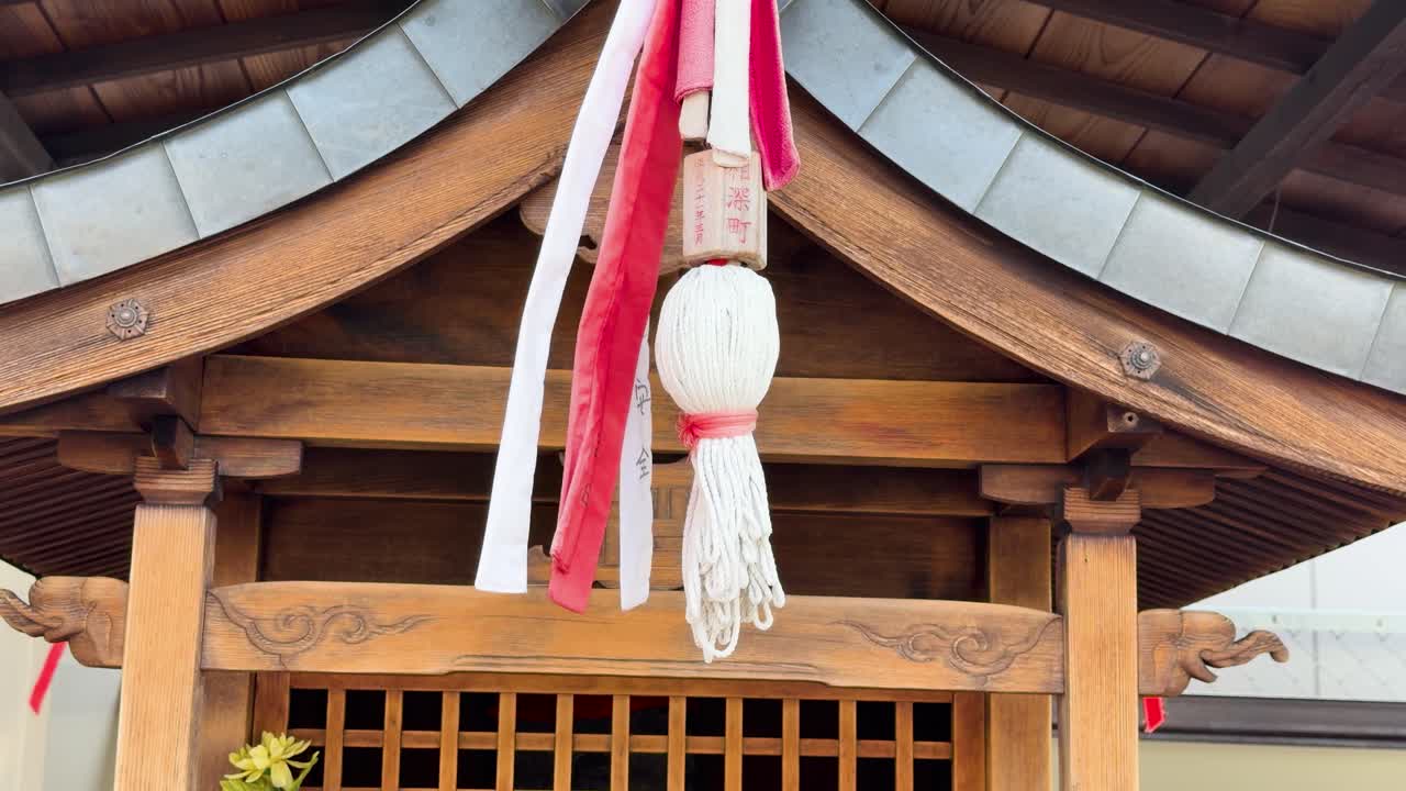 Static medium shot of a wooden Shinto shrine bell with red and white ropes