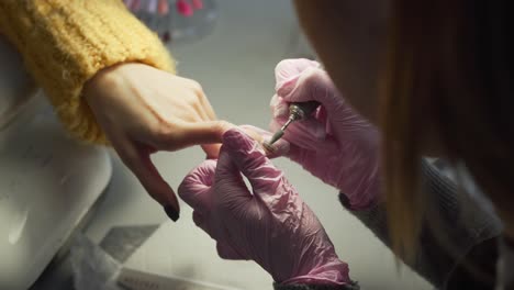 el experto en manicura usando guantes rosas quitando la laca de las uñas del cliente con un taladro de uñas