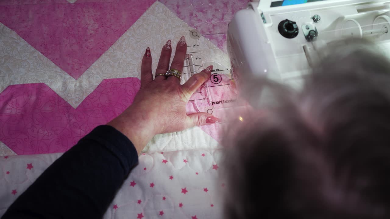 Woman using a sewing machine and a plastic template to sew a pattern on a quilt - over shoulder view