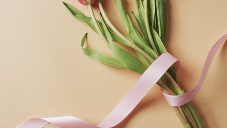 video of bunch of red tulips with pink ribbon and copy space on yellow background
