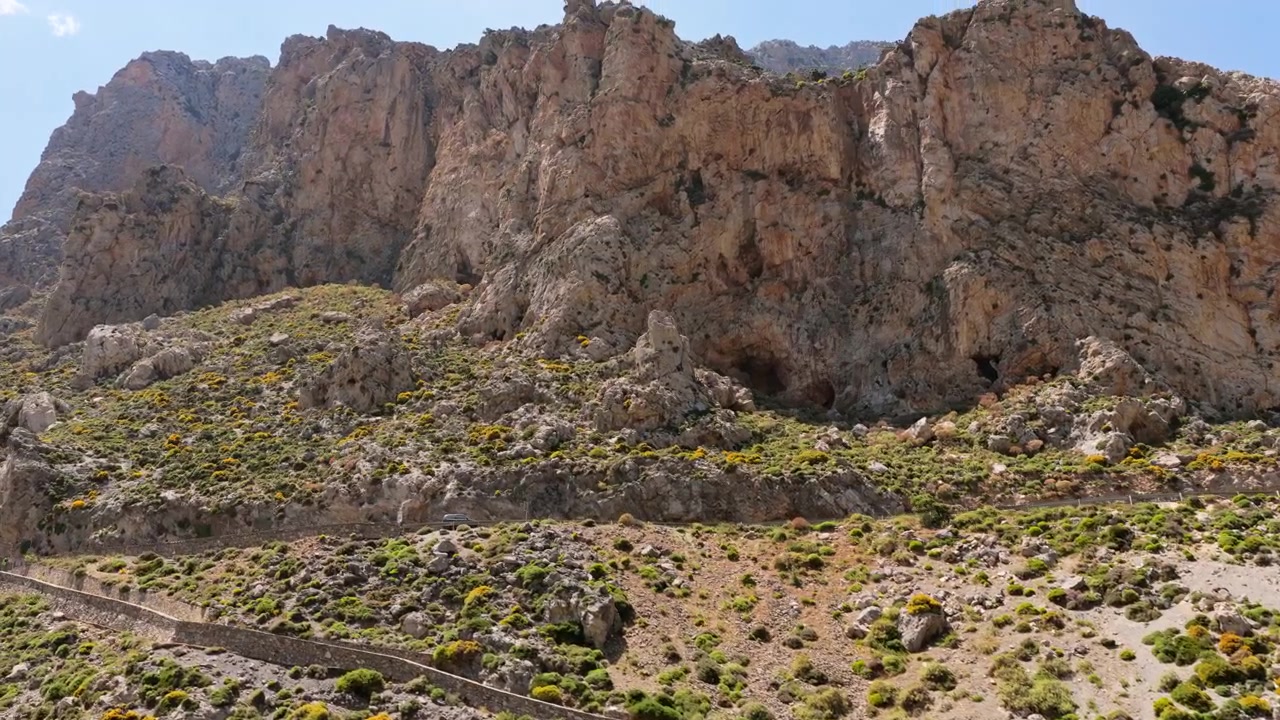Veduta aerea con drone di imponenti scogliere frastagliate che si ergono sopra una strada di montagna all'ingresso di una gola, Gola di Kourtaliotiko, Grecia