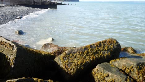 Sonnige-Blaue-Ozeanflut,-Die-Auf-Steinkiesstrand-Küstentourismus-Urlaubsszene-Wäscht