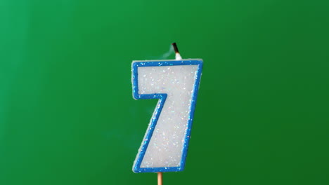 Seven-birthday-candle-flickering-and-extinguishing-on-green-background