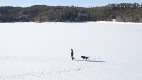 Man-Followed-By-His-Dog-Walking-In-The-Snowy-Land-On-A-Sunny-Winter-Day-In-Norway