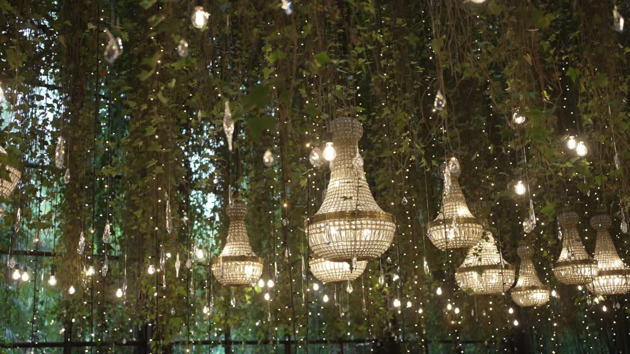 ornate chandeliers suspended among greenery and fairy lights in romantic event setting