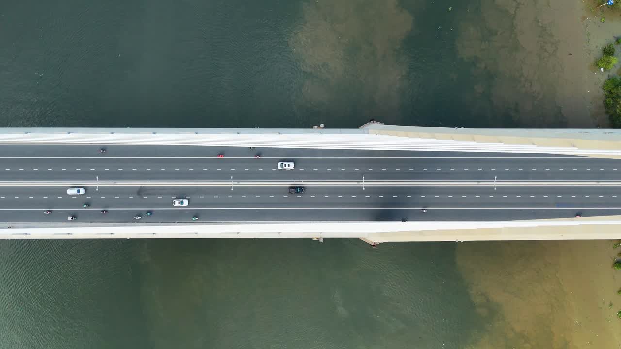 Top-down aerial view of a wide bridge spanning the Saigon River in Ho Chi Minh City, with light traffic crossing over calm waters. Vietnam, UHD.