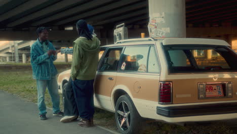 group of african american friends talking beside car parked under city bridge