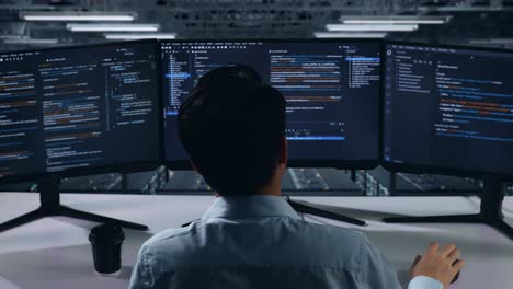 vista trasera de un desarrollador asiático que tiene dolor de cabeza mientras escribe código con múltiples pantallas de computadora en el centro de datos