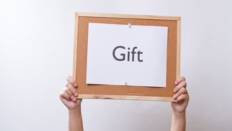 woman's hand shows the paper on board with the word gift in white studio background with copy space
