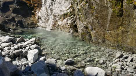 toma en cámara lenta de una cascada fresca que fluye hacia el río de la piscina clara durante el día soleado en la silla de montar gertrude, nueva zelanda