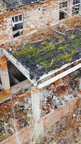 ruined brick buildings with collapsed roofs. broken dirt road with heaps of garbage. moss and grass on the ruins. aerial view. vertical video