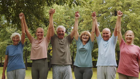 joyous senior people and female trainer posing with arms raised in park