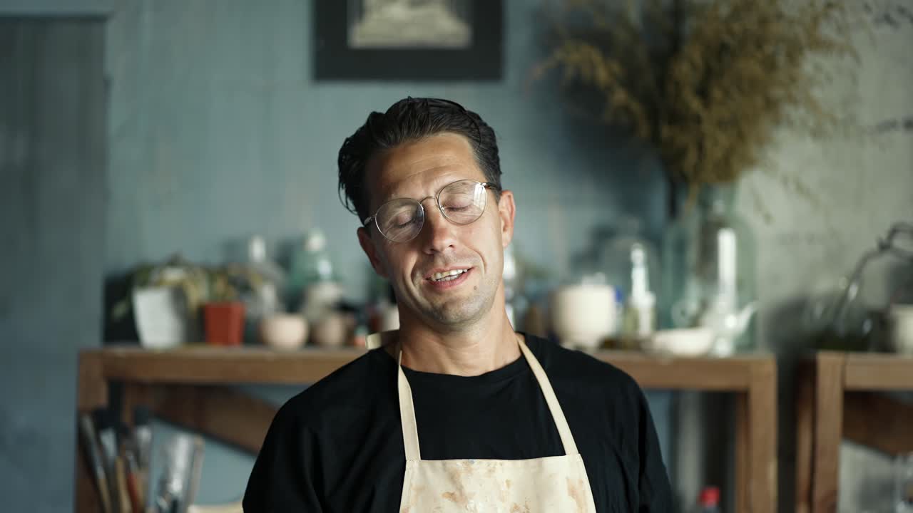 retrato de un joven alfarero feliz posando y poniéndose gafas. vídeo en primer plano