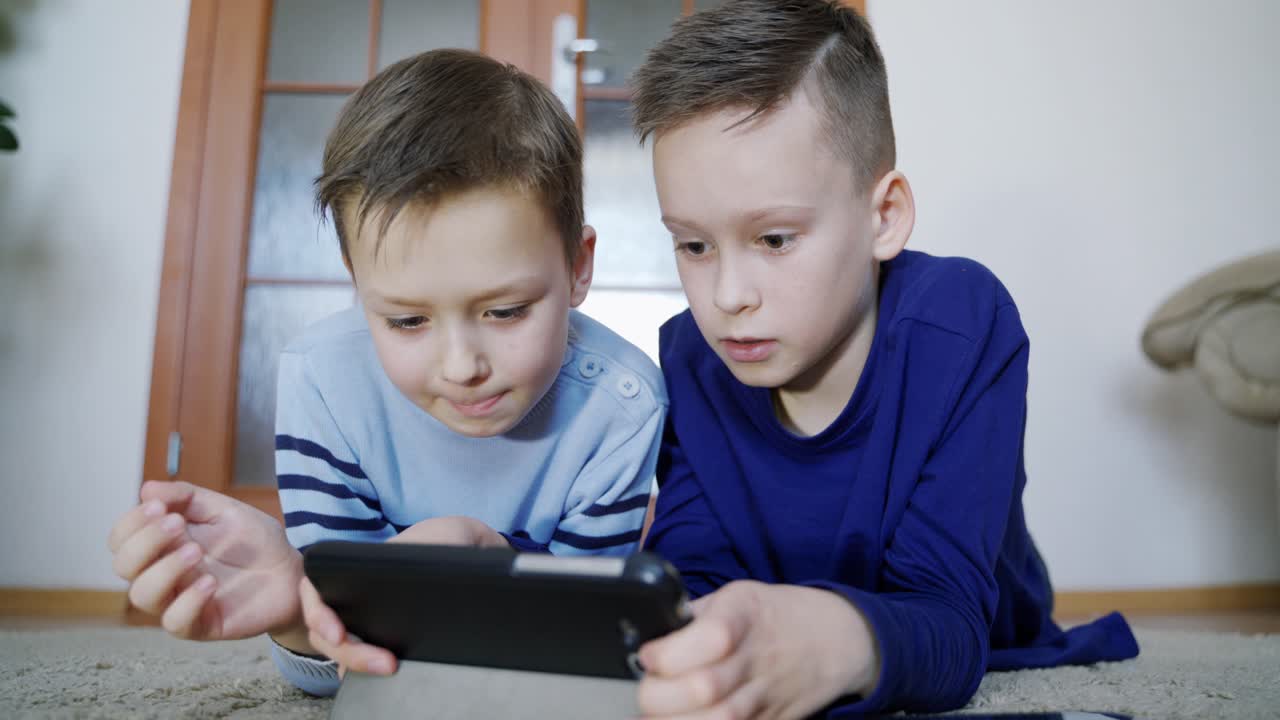 Brothers alone at home using mobile phone. Children playing video games on electronic gadget alone at home