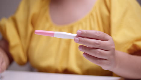 detail of woman in yellow dress checking pregnancy test together with calendar