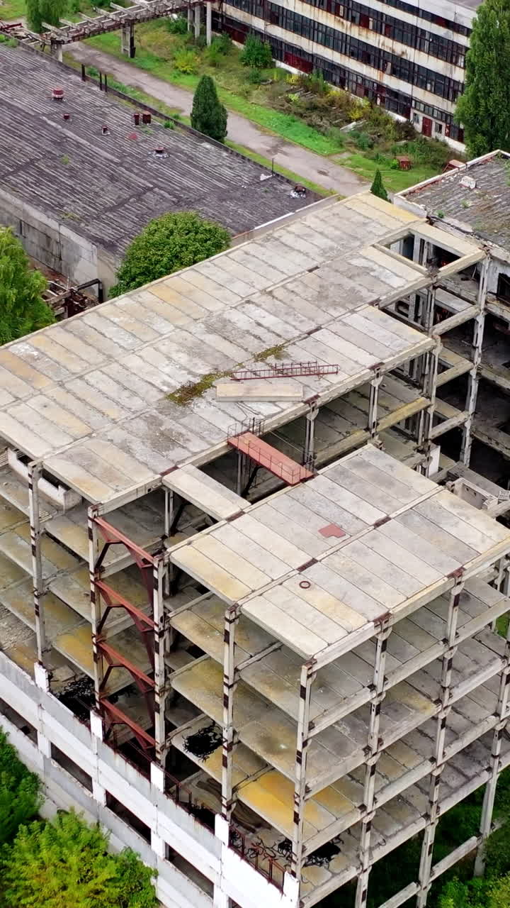 Unfinished old building without windows on a factory. Abandoned territory of industrial plant with empty buildings and warehouses. Aerial view.. Vertical video