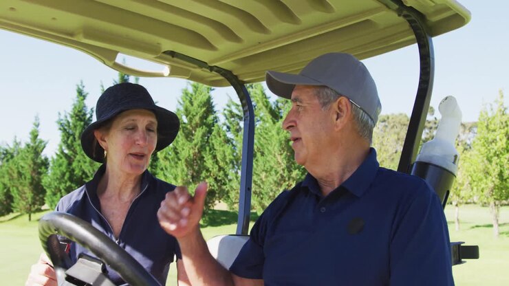 Coppia anziana caucasica che conversa mentre è seduta su un golf cart al campo da golf.