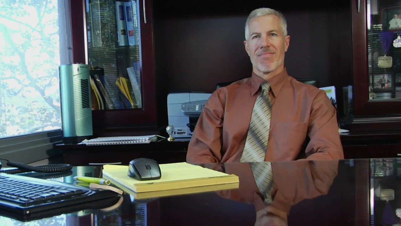 un hombre de negocios se inclina hacia adelante en su escritorio y junta sus manos