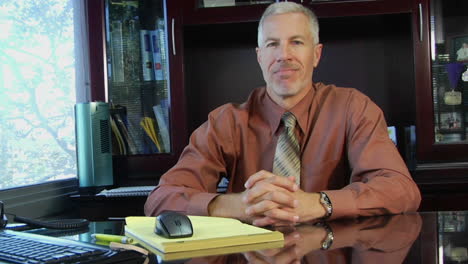 A-businessman-leans-forward-on-his-desk-and-clasps-his-hands-together