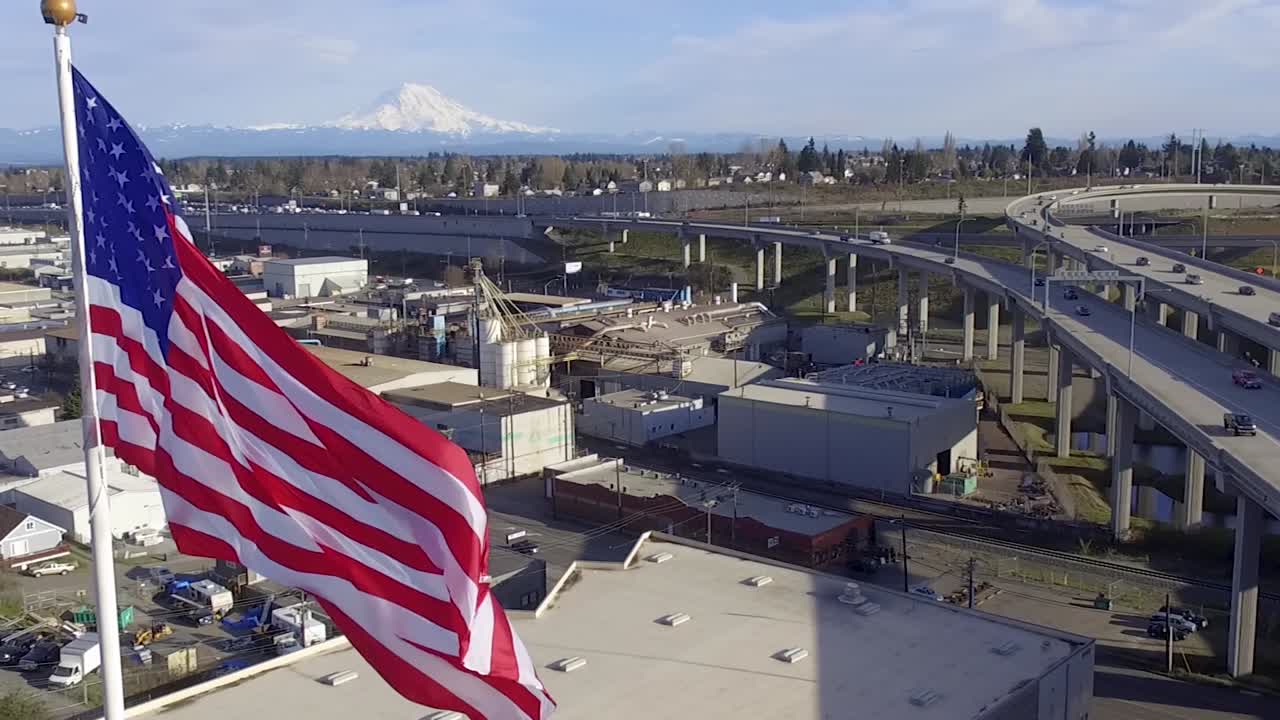 aerial, slow ascending shot of american flag waving above industrial valley with Mt Rainier on the horizon, Tacoma WA , USA