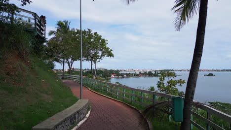 a drone mimics the movement of a person walking along a part of the path at mirante morro da cruz, passing through trees toward saquarema lagoon, with the city church in the background. wsl host.