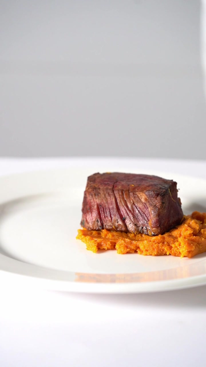Uno chef che impiattava una succulenta bistecca di manzo alla griglia servita su purè di verdure cremoso in un piatto minimalista, primo piano, inquadratura di dettaglio