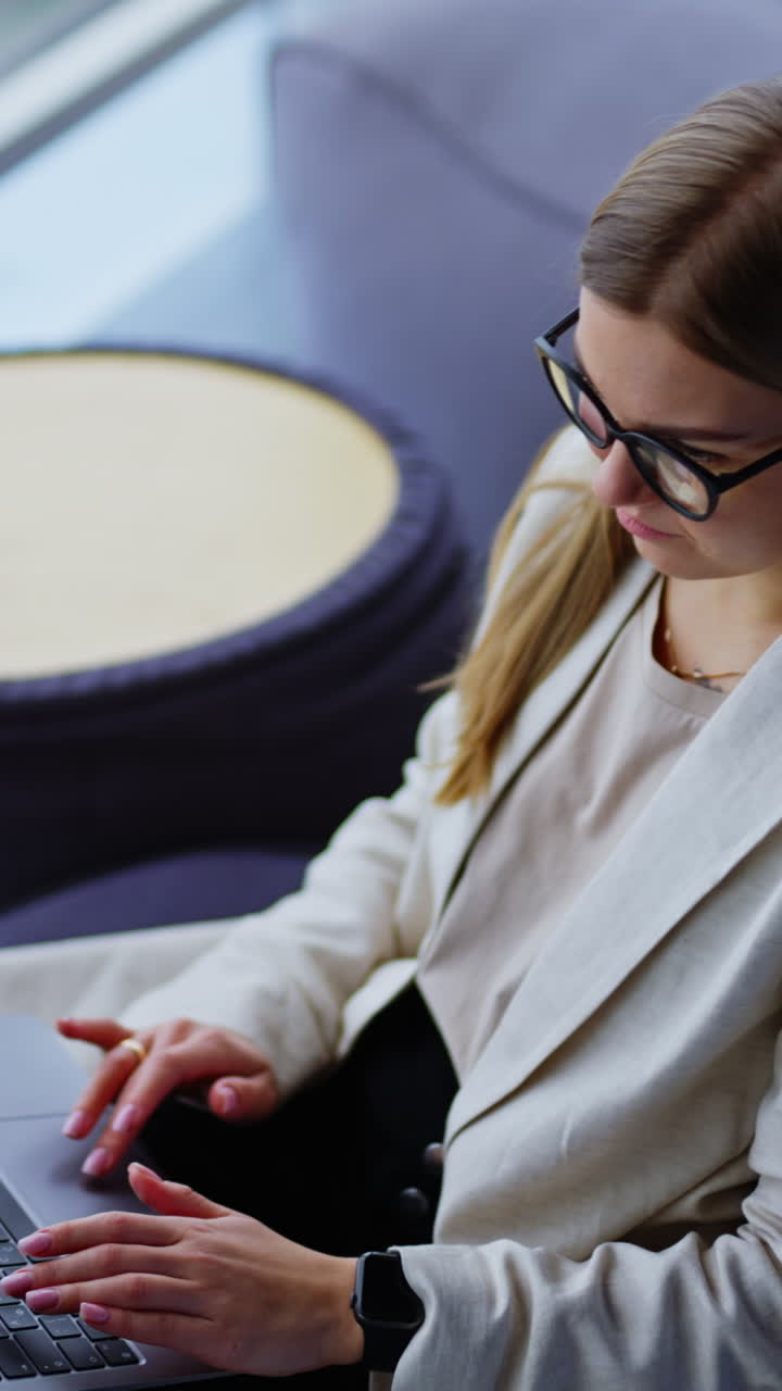 Calm relaxed young business lady working on laptop sitting in a chair. Freelance working lady in a comfortable place near big windows. Vertical video