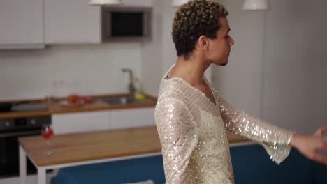 un hombre con un vestido se admira a sí mismo, bailando sensualmente en la cocina
