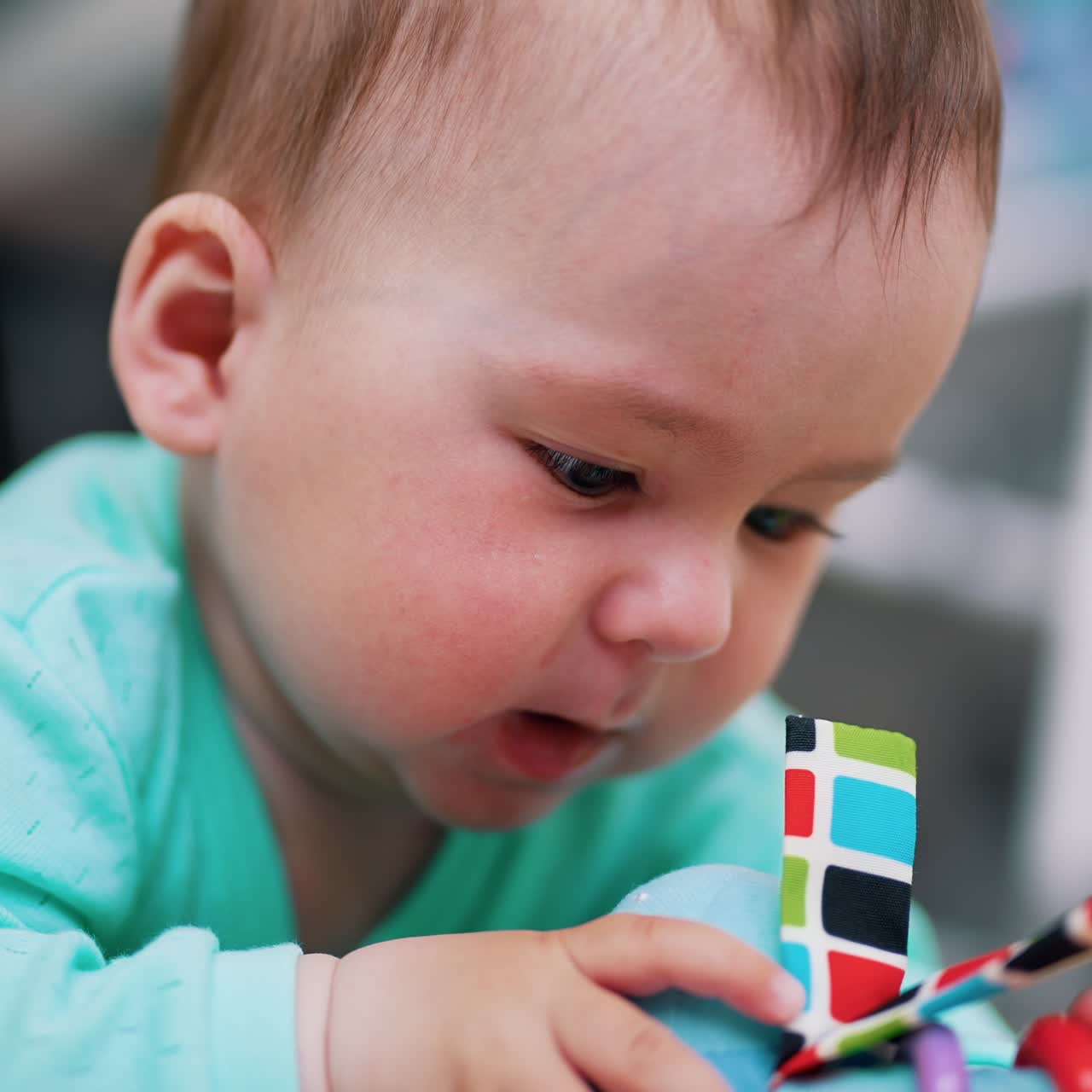 Darling little boy is busy playing with his toy. Child lies on belly waving with a toy. Close up. Blurred backdrop
