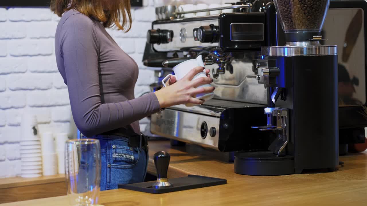 Professional barista preparing coffee. Professional barista holds metal jug while warming milk with a coffee machine
