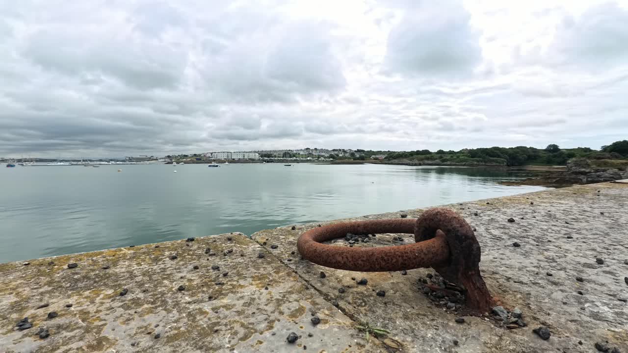 Storm clouds time lapse rolling across Holyhead harbour seafront beside rusted ships mooring ring