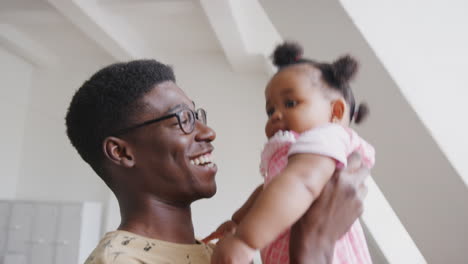 father playing game with baby daughter and lifting her in air in loft apartment