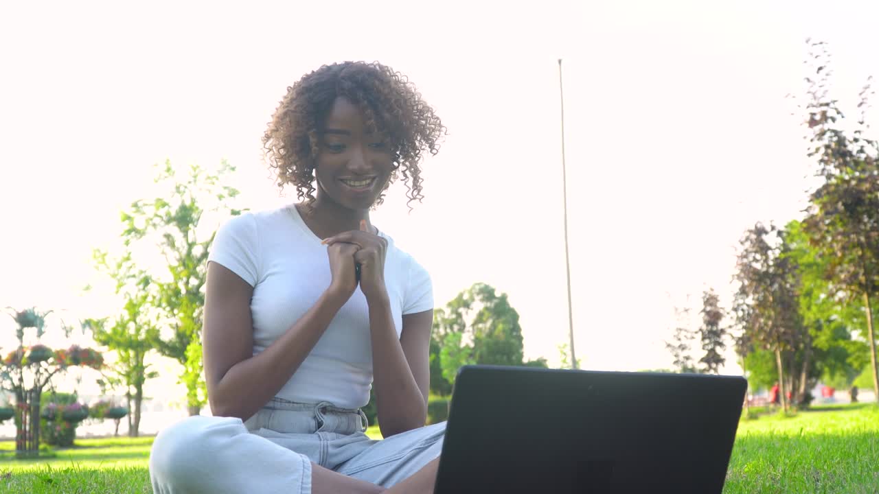 African american student e learning using computer webcam chat. Young woman calling on laptop talks with online teacher studying in the city park