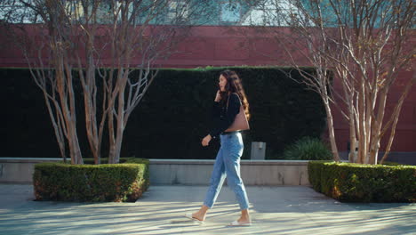 relaxed brunette walking street near green plants. asian girl going on pavement.