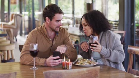 smiling mixed race couple using a smartphone together while having lunch at a restaurant