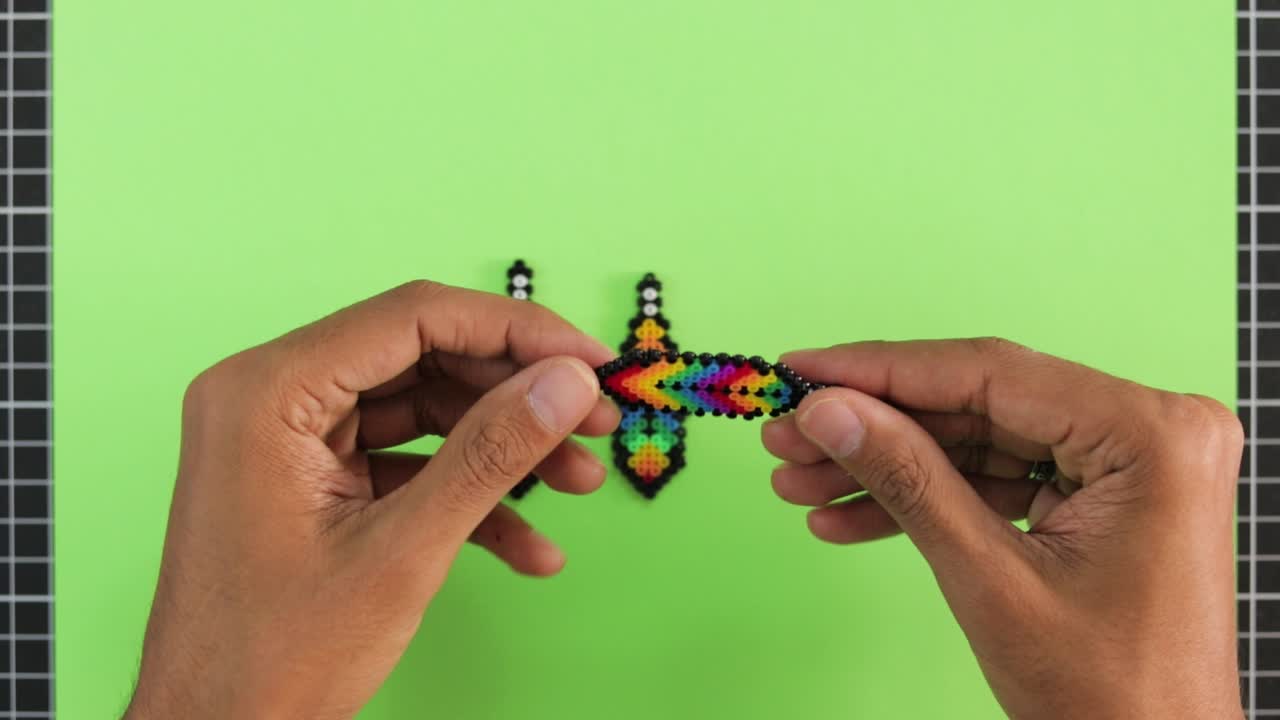 Hand arranging colorful bead earrings on a green background, craft concept
