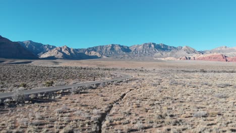 Aerial-drone-shot-of-Red-Rock-Scenic-Highway-with-mountains-in-the-background