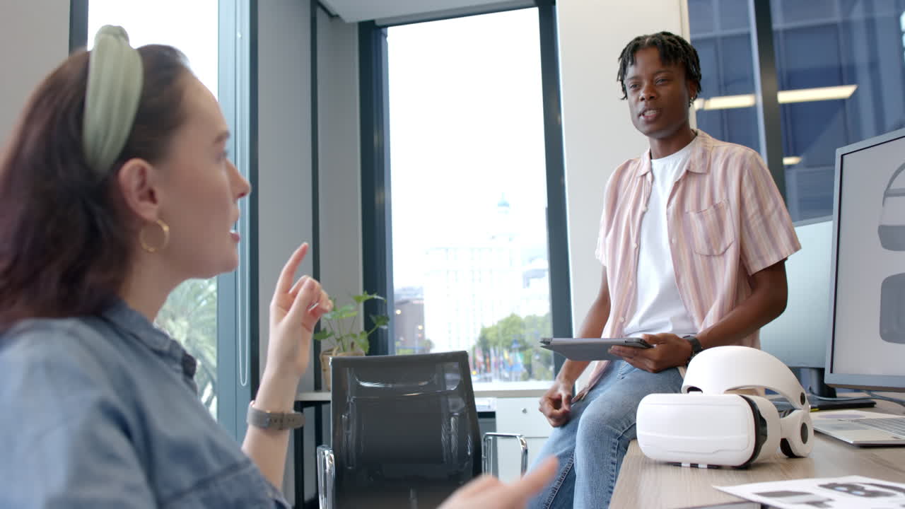 Discussing project, colleagues using tablet and VR headset in modern office setting