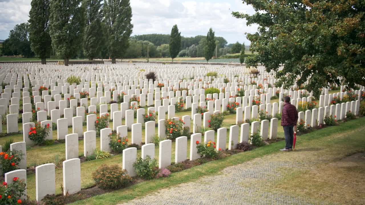Man looking and reflecting at War Memorial graves in a Cemetery in Ypres Belgium, amongst Green Garden with Red Roses