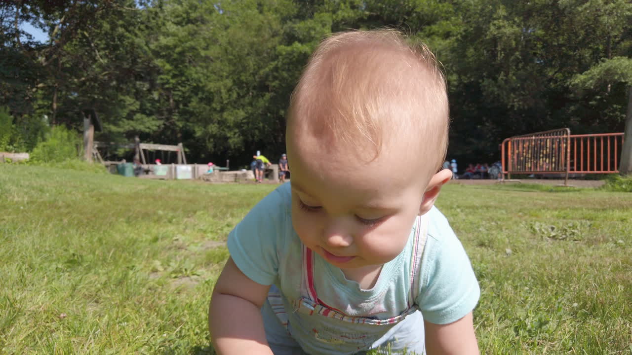 Babbling baby boy crawling through the grass toward the camera
