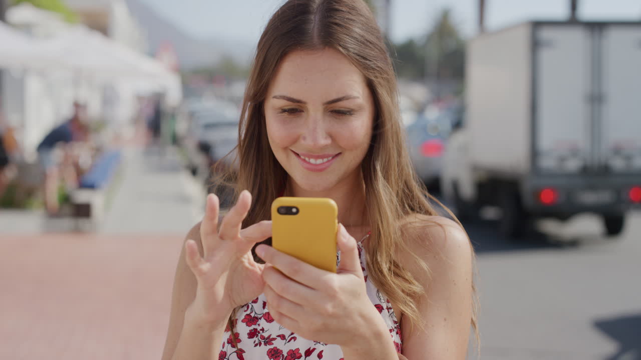 아름다운 젊은 여성 관광객의 초상화 스마트폰을 사용하여 문자 메시지를 보내고 온라인 브라우징을 즐기고 여름 휴가 경험을 공유하고 바쁜 해변에서 소셜 미디어 메시지를 보내고 있습니다.