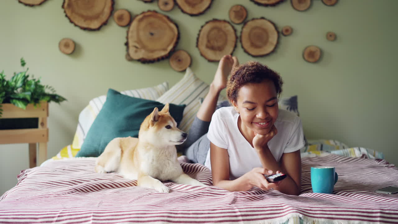 Young Woman Relaxing on Bed with Dog, Watching TV