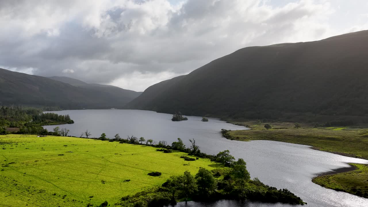 Drone camera pans across lush valley, reflective lake, and misty mountains under soft daylight