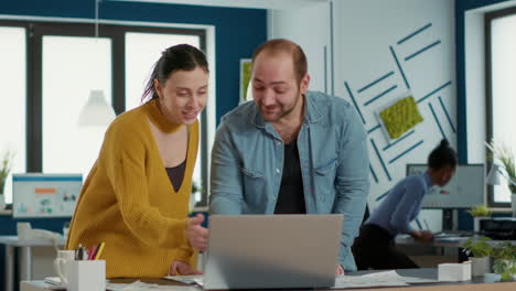 Smiling-coworkers-in-office-looking-at-laptop-screen-comparing-business-analytics-with-sales-charts