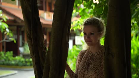 Hermosa-Joven-Modelo-Caucásica-Caminando-Por-El-Borde-De-La-Selva-Tropical-En-Denpasar-Bali-Indonesia-Con-La-Típica-Flor-Balinesa-En-El-Pelo-Con-La-Casa-De-Indonesia-En-El-Fondo