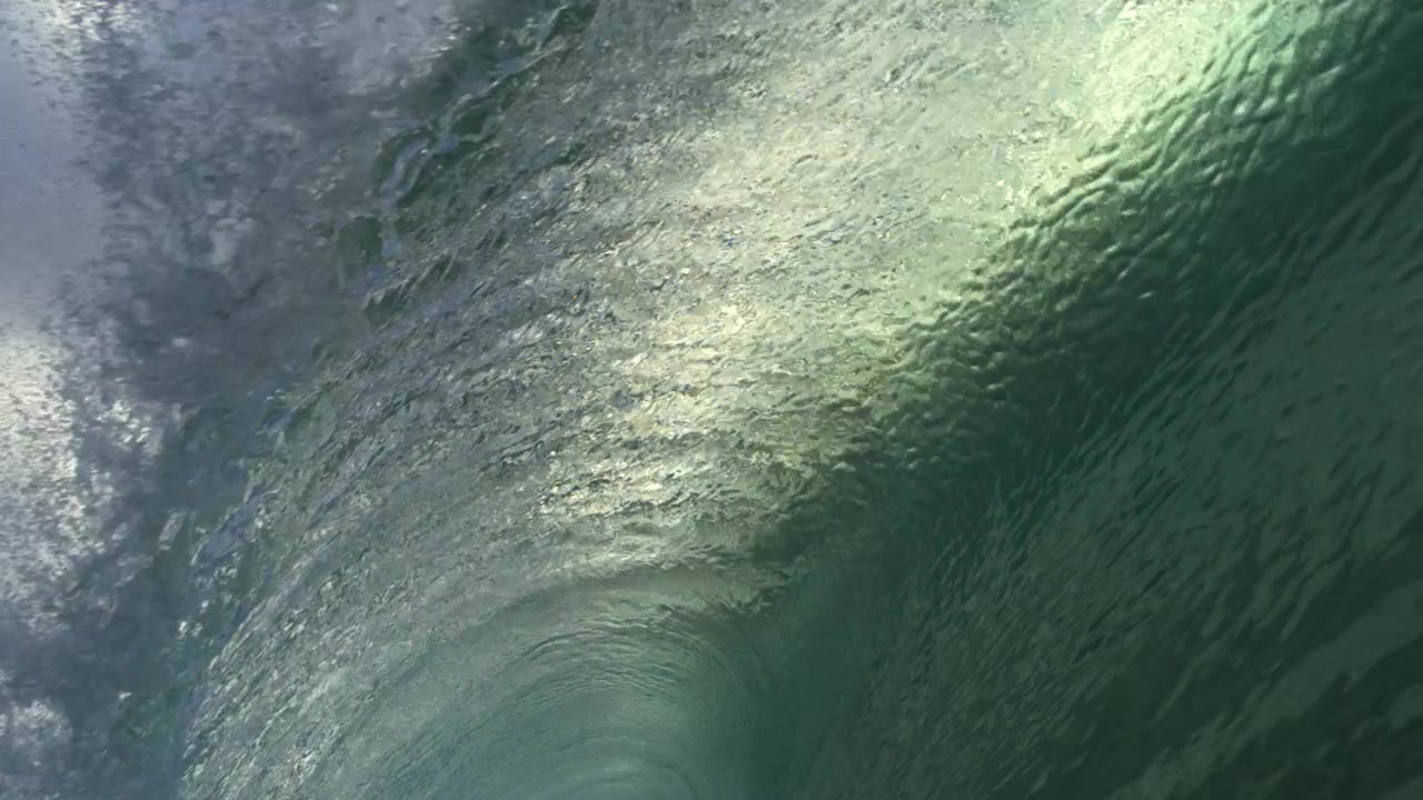Un'onda oceanica verde luminosa si arriccia sull'acqua scura sotto un cielo brillante, in un fluido slow motion.