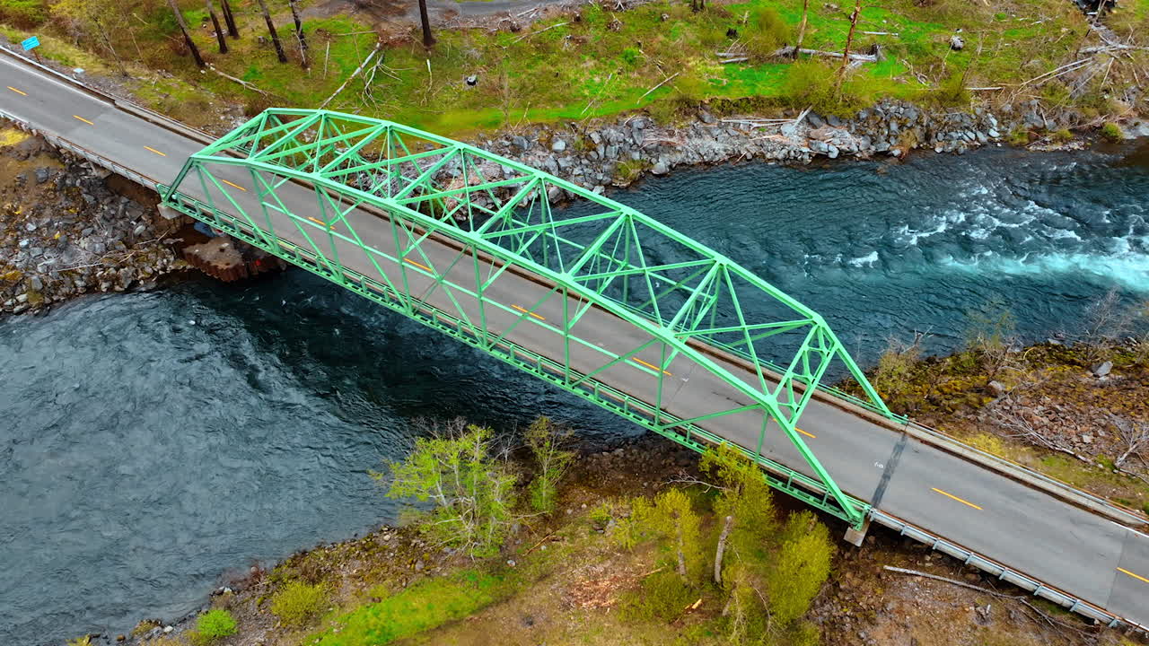 Bridge with a metal construction above narrow river. Some dry wood lies on the waterfront of the river. Top view.