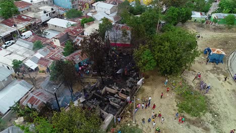 Aerial-view-of-firemen-calming-last-flames-in-a-burnt-house-fire,-cloudy-day,-in-Port-au-Prince,-Haiti---orbit,-drone-shot