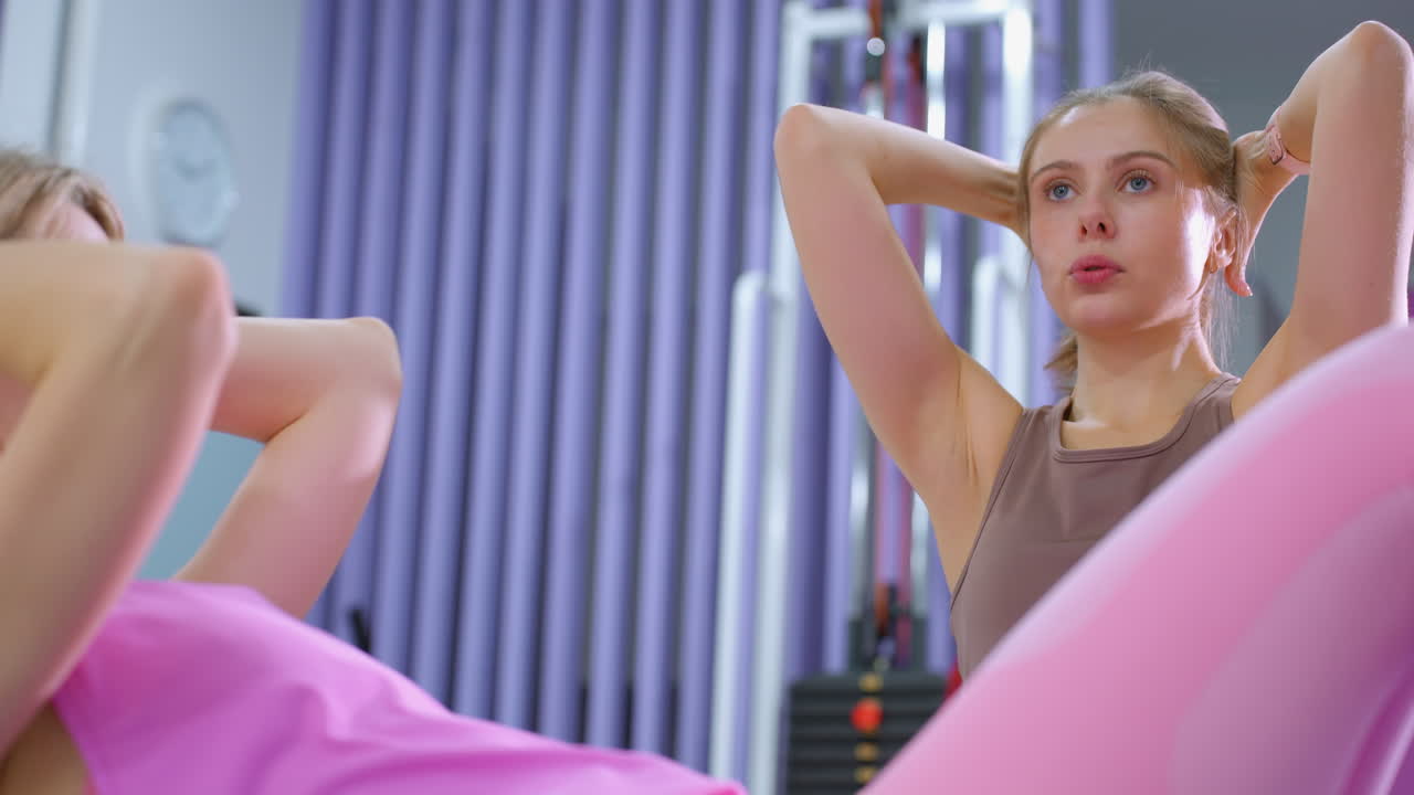 sesión de entrenamiento abdominal intenso con una mujer de color rosa haciendo abdominales con un instructor enfocado que proporciona orientación, en un gimnasio bien equipado
