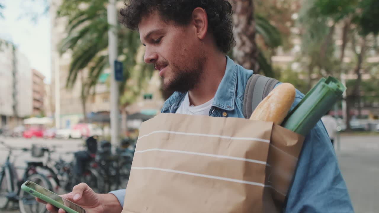 Man with groceries using his phone on the street